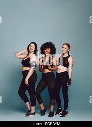 Gruppe von unterschiedlichen Frauen in Sportswear zusammen über grauer Hintergrund stehen. Drei Frauen verschiedener Gewicht in Fitness Kleidung. Stockfoto