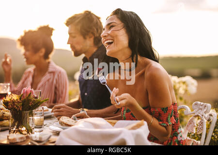 Lachen mit Freunden zu reden, während sie das Essen auf einer Party im Freien. Frau genießen mit Freunden bei einem Abendessen. Stockfoto