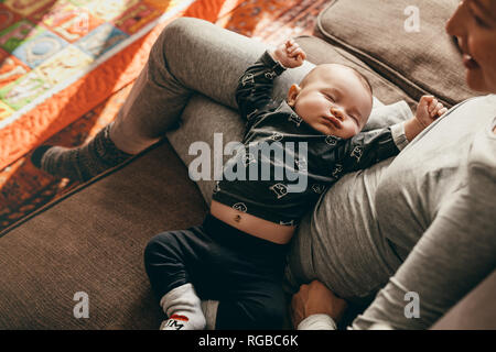Baby in einen tiefen Schlaf in den Schoß seiner Mutter zu Hause. Mutter sitzt auf der Couch, mit ihrem Baby schlafen in ihren Schoß. Stockfoto