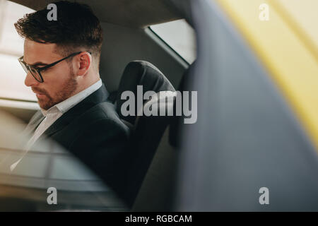 Business Person tragen Brillen sitzen auf dem Rücksitz eines Autos Büro gehen. Seitenansicht eines Kaufmanns im Auto sitzen auf der Suche beschäftigt. Stockfoto