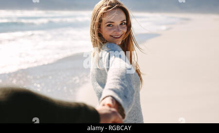 Schöne Frau zu Fuß entlang der Küste mit ihrem Freund. Frau die Hand ihres Mannes und lächelnd, während sie einen Spaziergang am Strand. Stockfoto