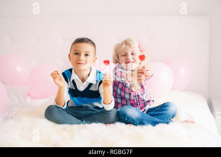 Group Portrait von zwei Glückliche weiß Kaukasischen cute adorable lustig Kinder essen herzförmige Lollis. Junge und Mädchen feiern Valentinstag. Liebe, Stockfoto