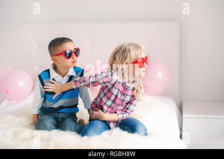 Porträt von zwei unglücklich weiß Kaukasischen cute adorable lustig Kinder tragen Herzform Gläser. Junge und Mädchen kämpfen und in einen Streit oder alahuhta Stockfoto