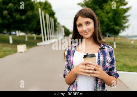 Jugendlicher Mädchen 10-14 Jahre alt, im Stadtpark, im Sommer, eine Tasse Kaffee oder Tee in den Händen. Im Sommer glücklich lächeln. Die Stockfoto