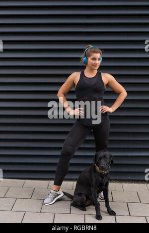 Porträt der jungen Frau mit Kopfhörer und Hund im Freien Stockfoto