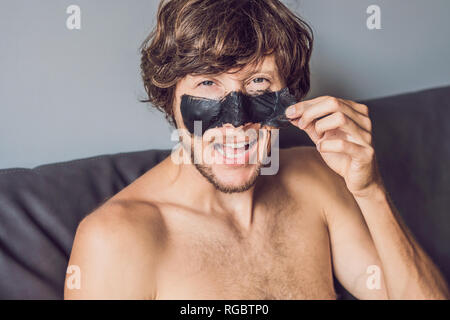 Glückliche Menschen mit schwarzer Maske auf dem Gesicht. Foto Mann empfangen von Wellnessanwendungen. Beauty Skin Care Concept Stockfoto