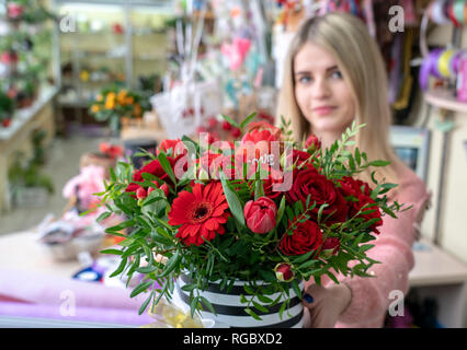 Ein Mädchen, ein Blumengeschäft - Designer hält aus einer schönen, festlichen Blumenstrauß aus roten Blumen und ein Herz mit der Aufschrift Liebe, speziell zum Valentinstag gemacht Stockfoto