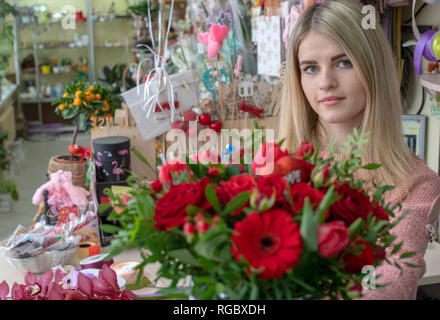 Ein Mädchen, ein Blumengeschäft - Designer hält aus einer schönen, festlichen Blumenstrauß aus roten Blumen und ein Herz mit der Aufschrift Liebe, speziell zum Valentinstag gemacht Stockfoto