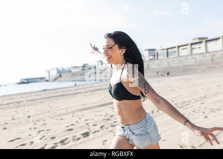 Glückliche junge Frau mit tattoo Laufen am Strand Stockfoto