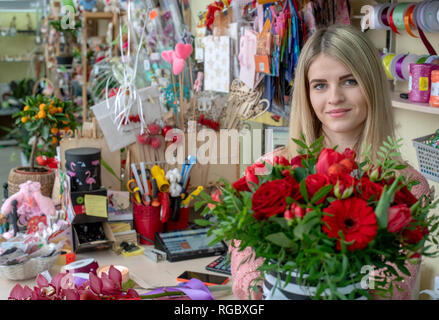 Ein Mädchen, ein Blumengeschäft - Designer hält aus einer schönen, festlichen Blumenstrauß aus roten Blumen und ein Herz mit der Aufschrift Liebe, speziell zum Valentinstag gemacht Stockfoto