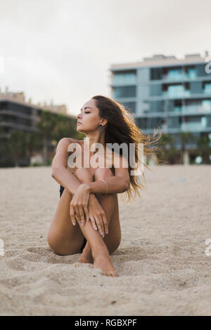 Schöne junge Frau sitzt am Strand bei Sonnenuntergang Stockfoto