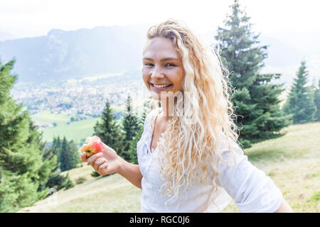 Deutschland, Bayern, Oberammergau, Portrait von lächelnden jungen Frau das Essen eines Apfels auf bergwiese Stockfoto