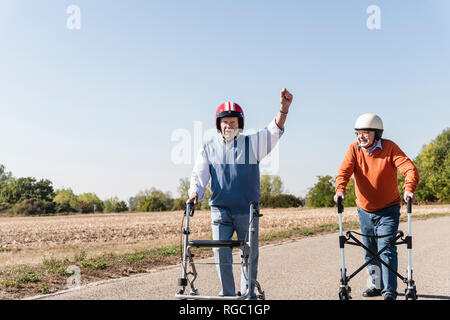 Zwei alte Freunde das Tragen von Schutzhelmen, konkurrieren in einem rollator Rennen Stockfoto