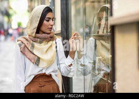 Spanien, Granada, junge muslimische touristische Frau mit Kopftuch in Shop Windows auf einer Einkaufsstraße Stockfoto