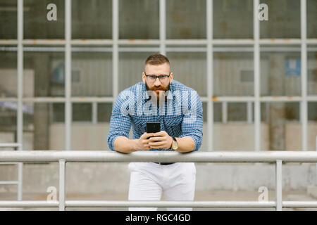 Portrait von bärtigen hipster Geschäftsmann mit Smartphone schiefen Zusatzscheinwerfer auf dem Dach Stockfoto