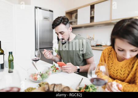 Man Kontrolle Nachrichten auf dem Handy, während dem Mittagessen mit seiner Freundin zu Hause Stockfoto