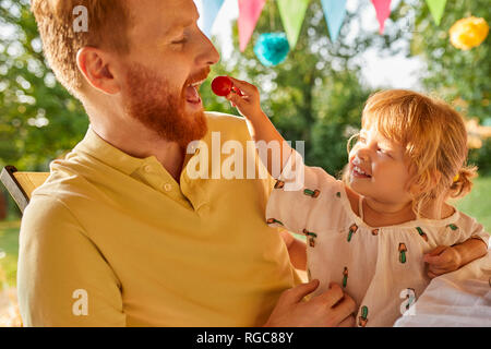 Tochter Fütterung Vater mit Tomaten auf einer Gartenparty Stockfoto