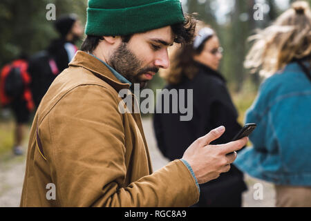 Man Kontrolle Handy im Freien mit Freunden im Hintergrund Stockfoto