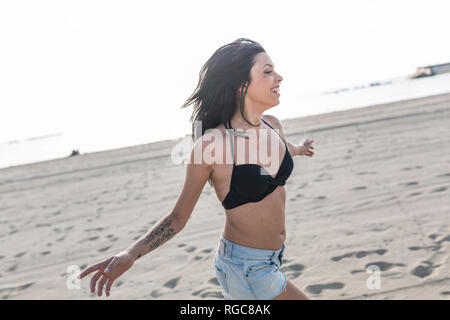 Glückliche junge Frau mit Tattoo und Piercing Nase läuft am Strand Stockfoto