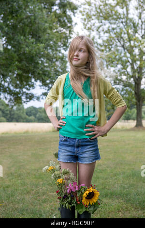 Portrait von blonde Mädchen stehen auf einer Wiese mit Blumen in ihrer Gummistiefel Stockfoto