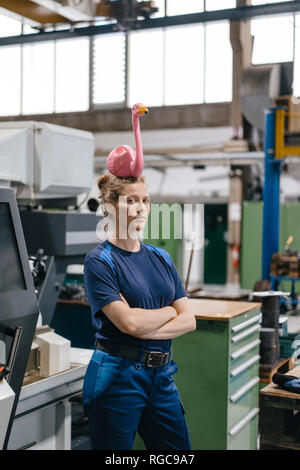 Junge Frau arbeiten als Facharbeiter in einem High-Tech-Unternehmen, das Auswuchten ein rosa Flamingo auf dem Kopf Stockfoto