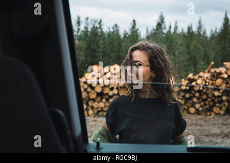 Junge Frau stand neben Auto neben Holz stapeln Stockfoto