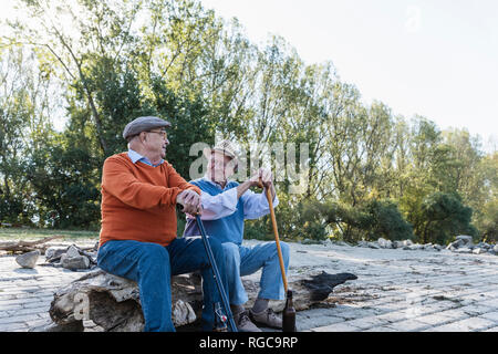 Zwei alte Freunde sitzen auf einem Baumstamm am Flussufer, Teilen von Erinnerungen Stockfoto