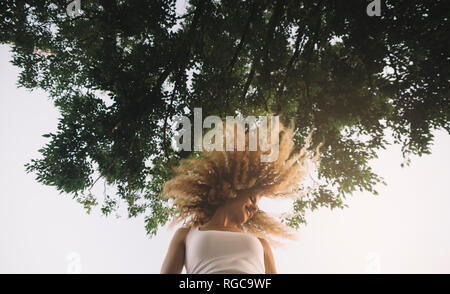 Junge Frau mit blonden Korkenzieherlocken stylen ihr Haar werfen Stockfoto