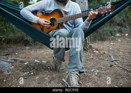 Mann in der Hängematte Gitarre spielen Sitzen im Wald, Teilansicht Stockfoto