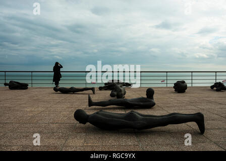 Das Dach des De La Warr Pavilion zeigt liegende Figuren von Antony Gormley, im Hintergrund eine Frau allein steht, wehmütig auf das Meer. Stockfoto