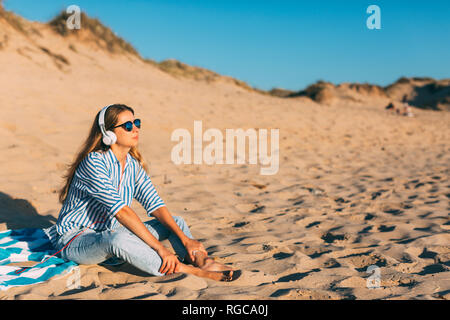 Portugal, Aveiro, Frau sitzt in der Nähe von Strand dune Musik hören mit Kopfhörern Stockfoto