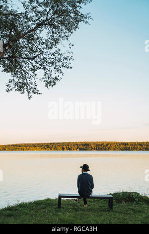 Junger Mann auf einer Bank sitzen, mit Blick auf den See Stockfoto