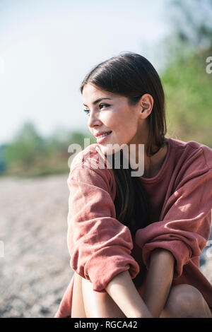 Lächelnde junge Frau sitzt im freien Stockfoto