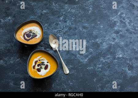 Zwei Schalen mit hausgemachten Hokkaido Kürbis Suppe, garniert mit Sahne, Kürbiskernöl und Kürbiskerne Stockfoto