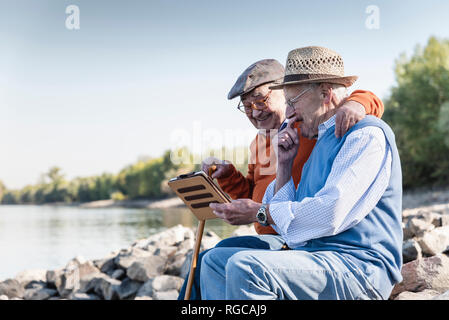 Zwei alte Freunde sitzen am Flussufer, mit digitalen Tablet Stockfoto