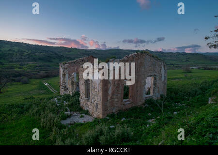 Die Sonne mit rosa Wolken auf einem Haus in einer ländlichen Gegend von Zypern ruinieren. Stockfoto