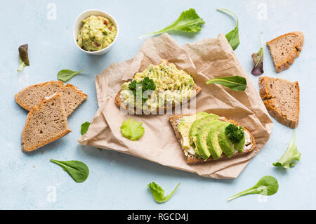 Scheiben Brot mit in Scheiben geschnittenen Avocado- und Avocado Creme auf braunem Papier Stockfoto