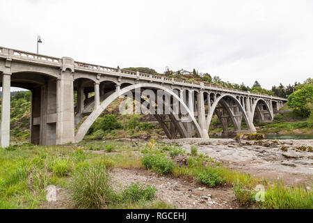 Eine konkrete Bogenbrücke überspannt das grüne Wasser im Süden Umpqua River in Oregon. Stockfoto