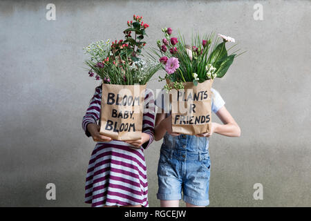 Zwei Mädchen Seite an Seite versteckt sich hinter Papiertüten mit Blumen Stockfoto