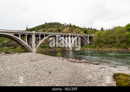 Eine konkrete Bogenbrücke überspannt das grüne Wasser im Süden Umpqua River in Oregon. Stockfoto