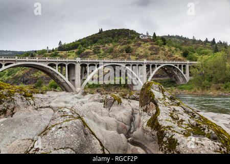 Wasser, zerklüfteten Felsen vor einem konkreten Bogenbrücke überspannt das grüne Wasser im Süden Umpqua River in Oregon. Stockfoto