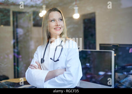 Lächelnde Frau Doktor mit Stethoskop hinter Fensterglas Stockfoto