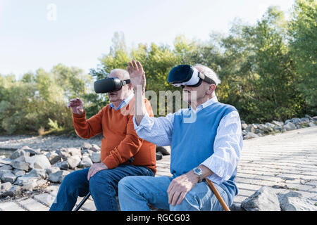 Zwei alte Freunde sitzen am Flussufer, mit VR-Brille Stockfoto