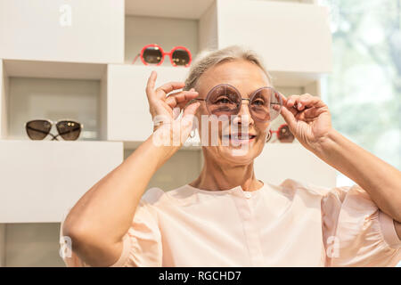 Lächelnde ältere Frau, die versucht, auf Sonnenbrille in einer Boutique Stockfoto