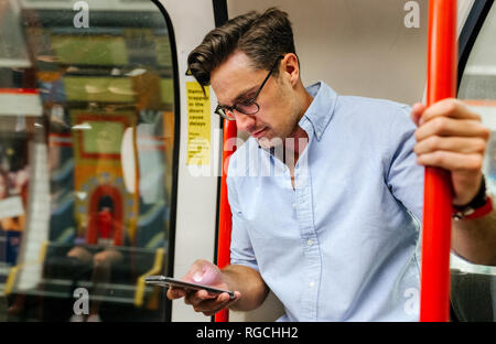 UK, London, Geschäftsmann, der in der U-Bahn an der Zelle Telefon Stockfoto