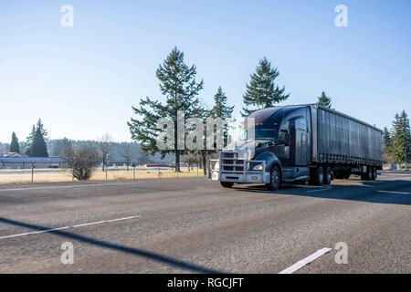 Dunkelgrau Big Rig amerikanischen Motorhaube, modernes, stilvolles Semi Truck mit starken Grill schutz Aluminium Stoßfänger und überdachte Auflieger auf dem breiten mu gehen Stockfoto
