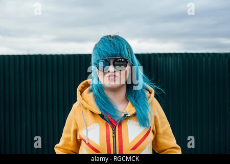 Porträt der jungen Frau mit blau gefärbtem Haar Sonnenbrille tragen und Hooded Jacket Stockfoto