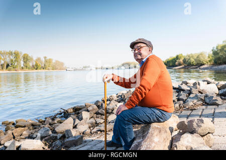 Alte Mann sitzt am Fluss Stockfoto