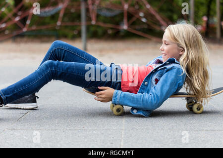 Lächelnde blonde Mädchen mit Skateboard auf dem Spielplatz Stockfoto