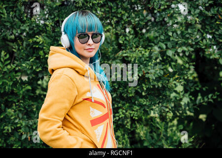 Porträt der jungen Frau mit blau gefärbten Haaren und Kopfhörer tragen gelbe Hooded Jacket Stockfoto